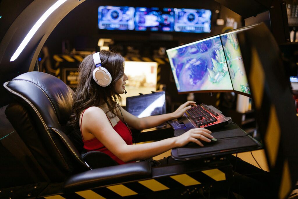Junge Frau mit Headset sitzt in einem ergonomischen Gaming-Stuhl und zockt an einem futuristischen Setup mit zwei Curved Monitoren.